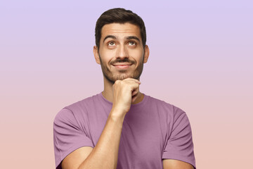 Young man in t-shirt with dreamy cheerful expression, thinking, looking up, isolated on purple