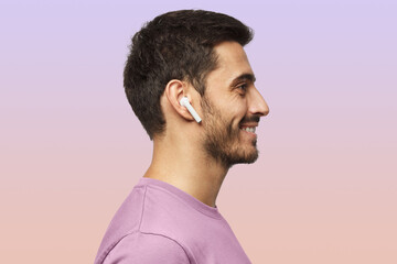 Sideways portrait of smiling young man listening to music or radio, uses modern wireless earphones - obrazy, fototapety, plakaty