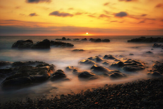 sunset over the sea, waves crashing on stones, long exposure