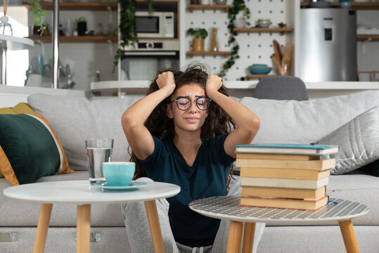 Young Frustrated School Girl Sitting On Floor With Pile Of Books Feeling Sad That She Need To Read. Female First Year College Student Get Depressed From How Much She Need To Study. Education Concept