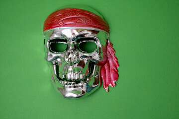 a silver skull with a red headband on a green background. Halloween, piracy. Jolly Roger. The sign...