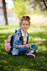 A sweet girl of five years on a walk. It's spring outside and the sun is bright. A girl holds a dandelion in her hands. She is wearing a colored T-shirt and a denim shirt. Childhood. Family.