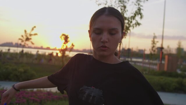 A young pretentious woman in a black t-shirt dances freestyle at an early sunset