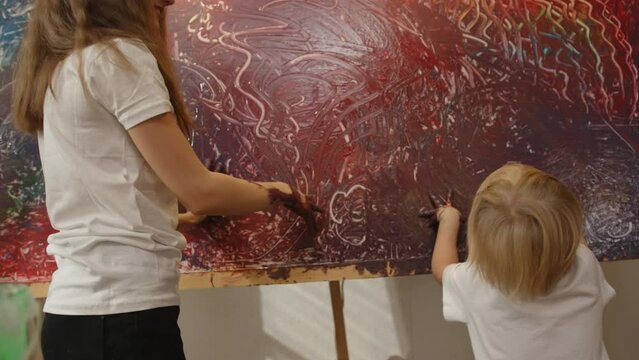 Girl 12 years old and child 4 years old draw picture with their hands in room using finger paints.