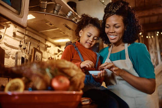 Happy African American mother and daughter enjoy while preparing Thanksgiving turkey for dinner in kitchen.