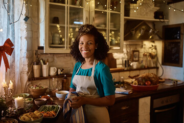 Happy black woman making Thanksgiving dinner in kitchen and looking at camera.