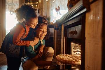 Happy African American mother and daughter taking out baked pie out of the oven in kitchen.