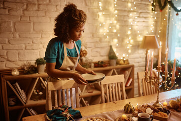 Black woman setting dining table for Thanksgiving lunch at home.
