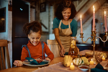Happy black daughter assisting her mother in setting dining table for family lunch on Christmas day,