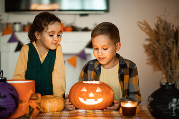 Young kid boy carving traditional Halloween jack-o-lanterns with scary face for party at home