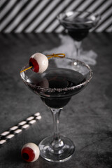 Halloween black cocktail in glasses with candy eyeball. Party festive celebrate concept.