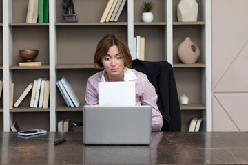 Tired frustrated and overworked business woman sitting in the office, holding documents and reading about problems in business