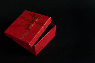 Still life red cardboard gift box with an opened lid and tied bow, isolated over black background with advertising copy space. Christmas or Valentine's Day concept. Boxing Day. Anniversary