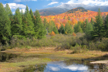 Autumn in White Mountains of New Hampshire. Scenic view of vibrant fall foliage and mountains in Franconia Notch State Park with fresh dusting of snow atop summit of Mount Lafayette.