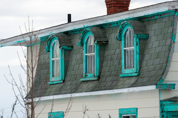 A vintage style white wooden building with teal blue trim, single casement windows, arch shaped...