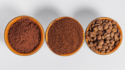 three small saucers with coffee beans, ground coffee and cocoa on a white background.