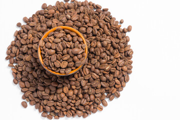 A small saucer with coffee beans stands on a pile of coffee on a white background.