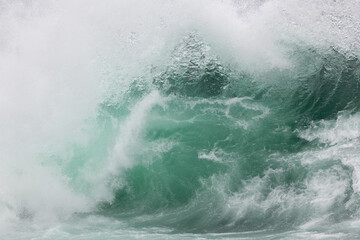Fototapeta na wymiar An angry teal green color massive rip curl of a wave as its barrel rolls along the ocean. The white mist and foam from the wave are foamy and fluffy. The ocean spray is coming off the top of the wave
