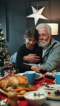 Vertical shot of a grandfather hugging his granddaughter while sitting at the table during Christmas lunch