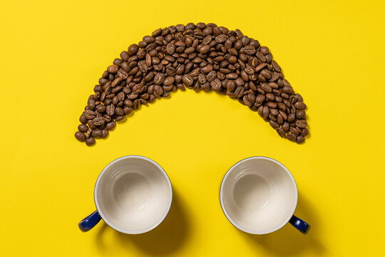Happy emoticon made of coffee beans on a yellow background.