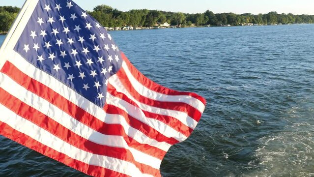 American flag waving in the breeze created by a moving cruise boat. Boating and lake footage begins looking down at water then tilts up. Hand held slow motion.
