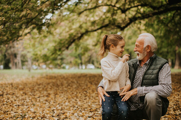 Grandfather spending time with his granddaughter in park on autumn day - obrazy, fototapety, plakaty
