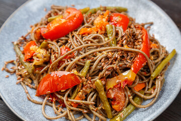 Soba with vegetables in soy sauce with spices in a plate close-up.