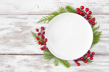 Christmas or winter table setting mock up. Blank white plate with frame of evergreen branches and...