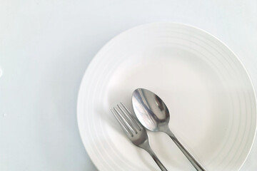 Spoon and fork in a white plate; White table in the restaurant with empty dish