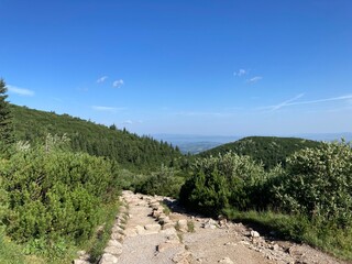 Summer day blue sky mountains landscape. Nature landscape with sun and blue sky. Summer travel in Europe mountains. Nature, lake, forest, trees hiking path. Clouds on blue sky. Forest landscape hiking