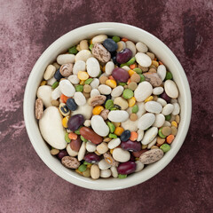 Top view of 13 bean soup ingredients in a white bowl on a maroon table.