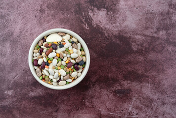 Top view of 13 bean soup ingredients in a white bowl offset on a maroon table.