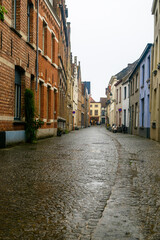 Fototapeta na wymiar Ancient street with cobblestones under the rain in Bruges, Belgium.