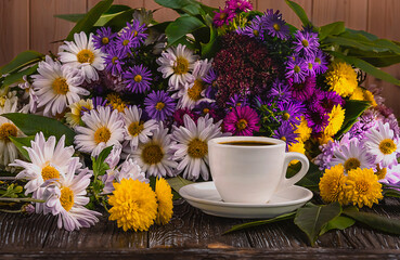 A white cup of coffee and a colorful bouquet of autumn flowers on a wooden background. Side view.