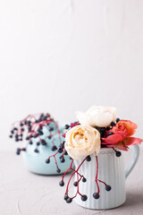 Postcard with lovely fall roses and wild blue berries in blue jur on light background. Selective focus. Still life. Romantic postcard. Place for text..