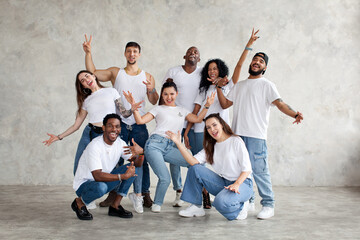 Multiethnic group of happy friends smile and raise hands up. Diverse young people standing together in white shirts and jeans on background wall in studio - Powered by Adobe