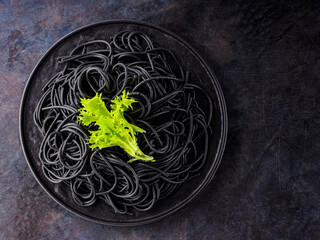 Black spaghetti with cuttlefish ink on a dark background. Cooked black spaghetti pasta with green lettuce. Top view. Copy space