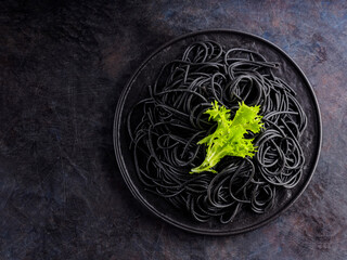 Black spaghetti with cuttlefish ink on a dark background. Cooked black spaghetti pasta with green lettuce. Top view. Copy space