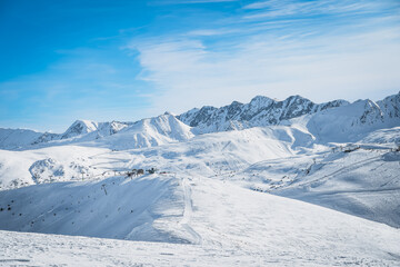 Ski lifts, skiers and snowboarders on pistes in beautiful winter scenery with mountain range in the...