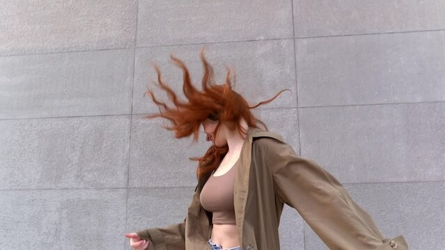 Happy teen redhead hipster girl wearing headphones listening music, dancing, jumping having fun in the city street at urban wall. Happy free teenage model enjoying digital music mix jumping outdoors.