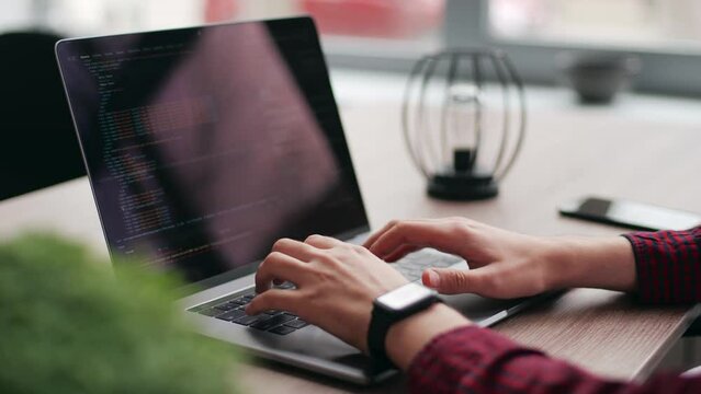 Close up of freelancer's hands typing code on laptop keyboard. Camera slides around developer's figers writing program code on computer display. Programmer working on online application database.