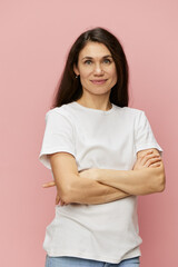 Fototapeta premium portrait of a cute, attractive woman on a pink background in a clean white t-shirt smiling pleasantly at the camera and folding her arms on her chest