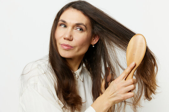 beautiful nice woman combing her long well-groomed hair with a wooden massage comb standing on a light background in a white shirt. horizontal photo
