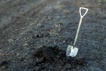 a shovel is inserted into the soil, next to it is loose excavated earth