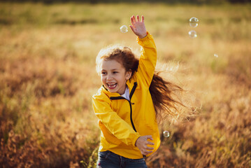 A cute girl of 5 years in a yellow park plays and has a fun with soap bubbles at sunset. Childhood. Sunlight. Rest with the family in nature.