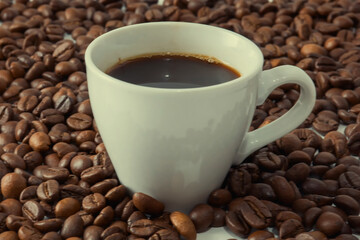 Coffee beans on a black background with a white cup.