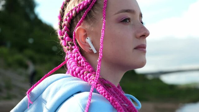 Portrait of a caucasian teenage girl with pink braids and wireless headphones in her ears on a deserted beach.Generation Z style.