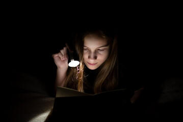 A teenage girl reads in the dark with a flashlight.