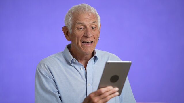 Elderly Having Video Chat Using Digital Tablet Computer Screen. Retired Old Man Spend Time Talking To Friends And Family Isolated On Solid Purple Background