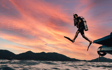 Scuba Diver Jumping to the open ocean on a background sunset doing giant jump